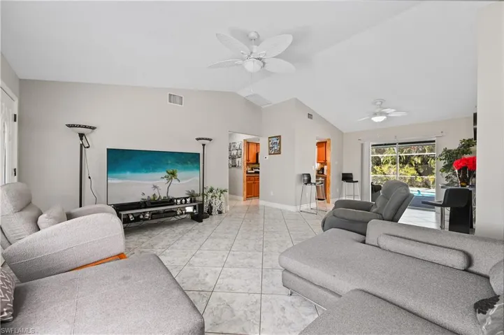 Living area featuring vaulted ceiling, light tile patterned flooring, and ceiling fan