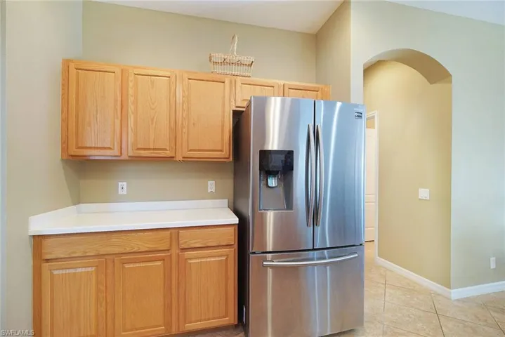 Kitchen with stainless steel fridge, light countertops, arched walkways, light tile patterned flooring, and light wood finish cabinetry