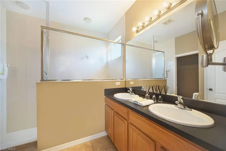 Full bath with double vanity, a spacious closet, a tile shower, and light tile patterned flooring
