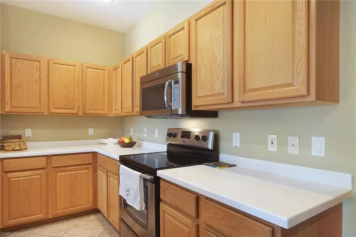 Kitchen with stainless steel appliances, light countertops, light tile patterned flooring, and light wood finish cabinetry