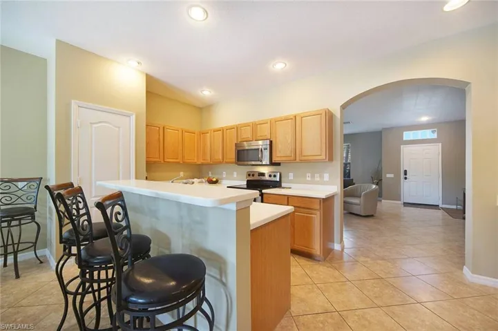 Kitchen with arched walkways, a center island with sink, light countertops, stainless steel appliances, and a breakfast bar