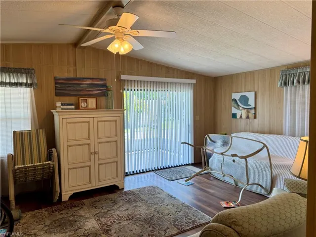 Living room with wooden walls, dark wood-style floors, and a ceiling fan