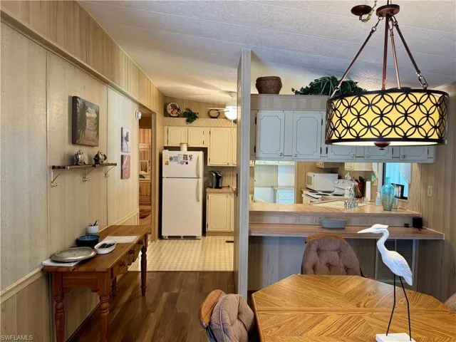 Kitchen featuring pendant lighting, dark wood-type flooring, wooden walls, white appliances, and a breakfast bar