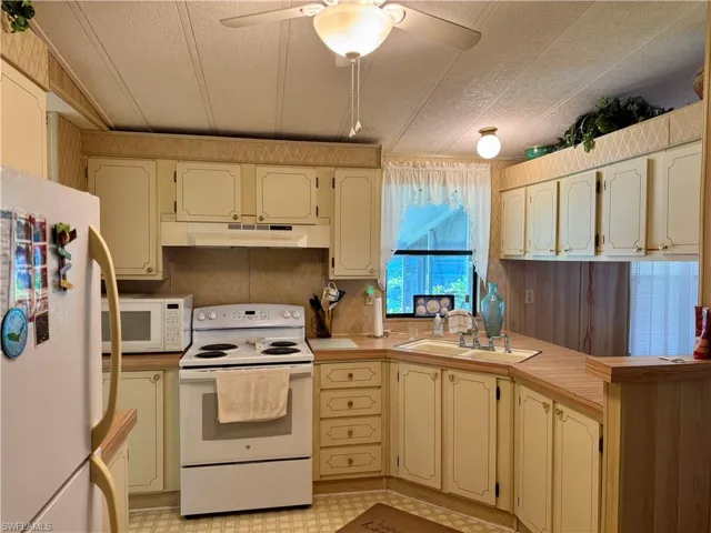 Kitchen with white appliances, light countertops, a peninsula, under cabinet range hood, and a textured ceiling