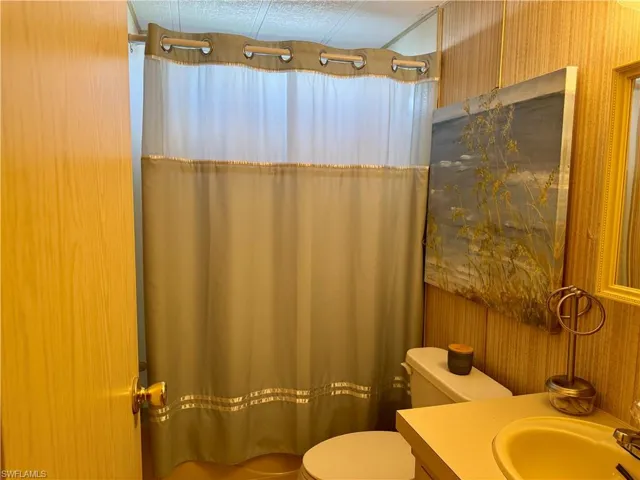 Full bathroom featuring wallpapered walls, vanity, and a textured ceiling