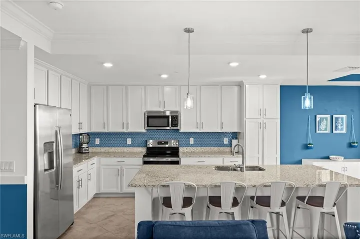 Contemporary kitchen featuring a spacious island with seating, white shaker cabinetry, stainless steel appliances, a blue geometric tile backsplash, and recessed lighting