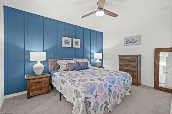 Accent wall with vertical paneling, crown molding, light gray carpet flooring, ceiling fan with integrated lighting, and white baseboards