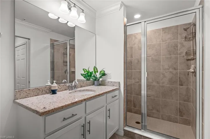 Bathroom featuring a spacious walk-in shower with tile surround, a single vanity with stone countertop, and a large mirror