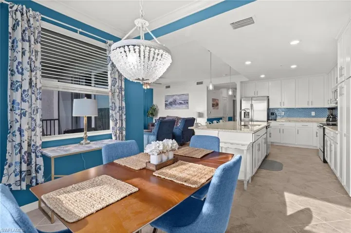Open-concept kitchen and dining area featuring a crystal chandelier, white cabinetry, stainless steel appliances, and a kitchen island with seating