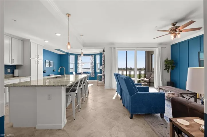 Open-concept living space featuring a kitchen with white cabinetry and a large island, a dining area with bay windows, and a living room with a decorative accent wall