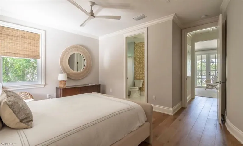 Bedroom with ornamental molding, multiple windows, hardwood / wood-style floors, a ceiling fan, and ensuite bathroom
