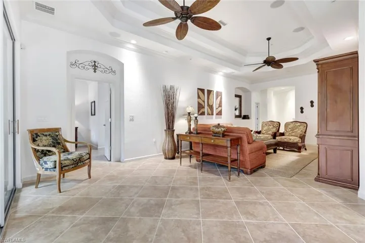 Living area featuring crown molding, a raised ceiling, arched walkways, ceiling fan, and light tile patterned floors