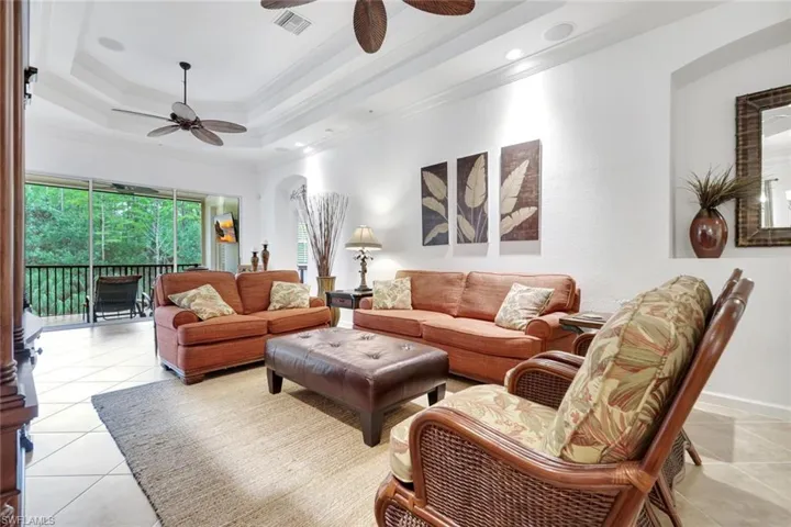 Living room with light tile patterned floors, a tray ceiling, ornamental molding, and a ceiling fan