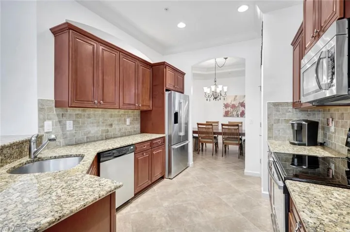 Kitchen with appliances with stainless steel finishes, tasteful backsplash, light stone counters, decorative light fixtures, and a chandelier