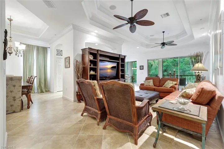 Living room with a tray ceiling, ornamental molding, light tile patterned floors, ceiling fan, and a chandelier