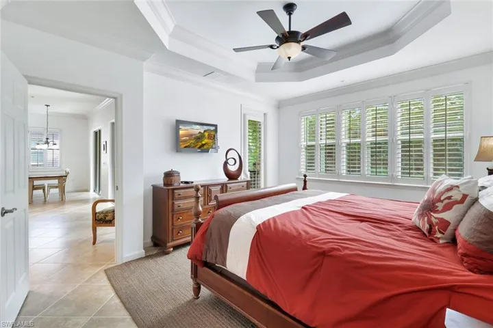 Bedroom featuring crown molding, multiple windows, tile patterned floors, a ceiling fan, and a raised ceiling