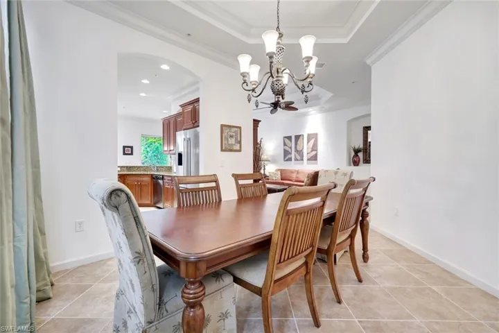 Dining area with arched walkways, light tile patterned floors, ornamental molding, a chandelier, and a tray ceiling