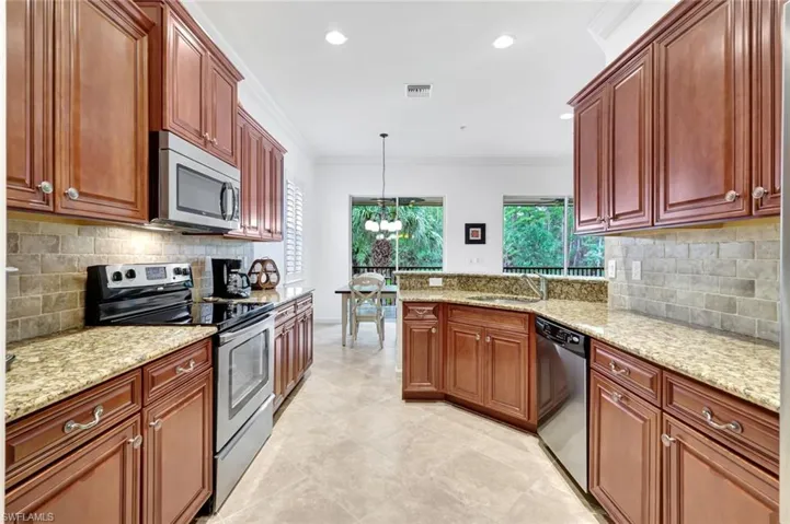Kitchen with decorative backsplash, appliances with stainless steel finishes, ornamental molding, hanging light fixtures, and a chandelier