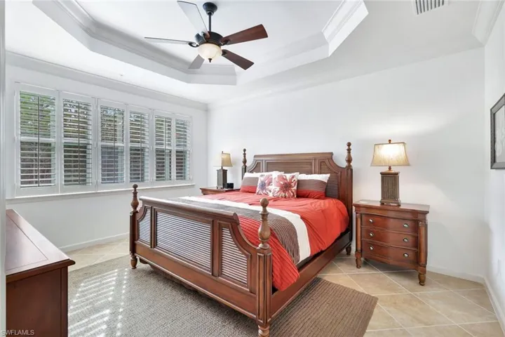 Bedroom with ornamental molding, light tile patterned flooring, ceiling fan, and a raised ceiling