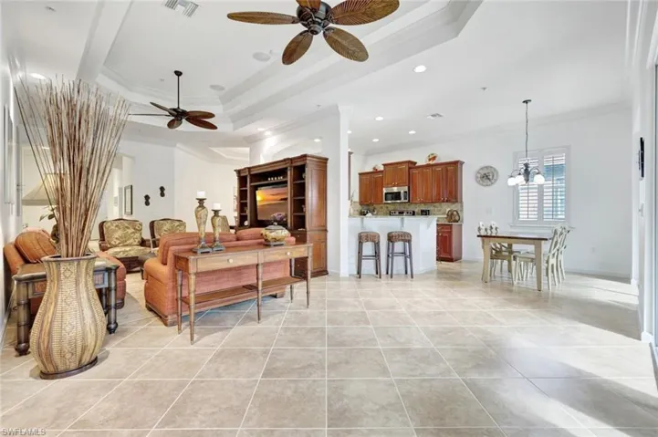 Living room with crown molding, a tray ceiling, a ceiling fan, a chandelier, and light tile patterned flooring