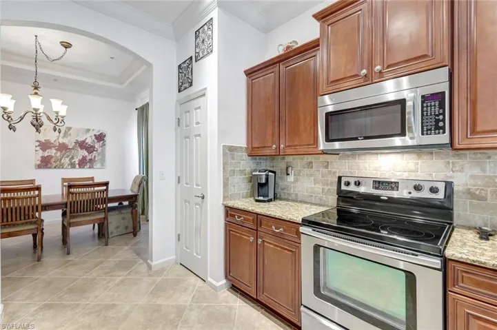Kitchen featuring appliances with stainless steel finishes, ornamental molding, hanging light fixtures, arched walkways, and light stone countertops