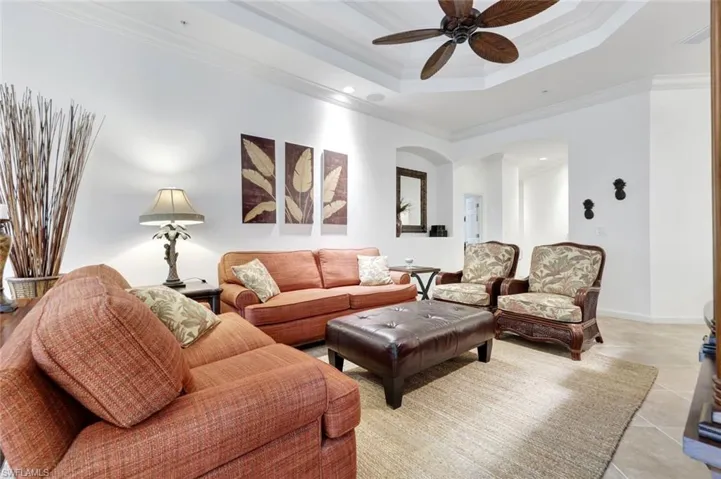 Tiled living room featuring a raised ceiling, ornamental molding, ceiling fan, recessed lighting, and arched walkways