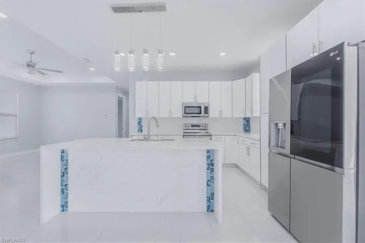 Kitchen featuring stainless steel appliances, a kitchen island with sink, white cabinetry, decorative light fixtures, and light stone counters