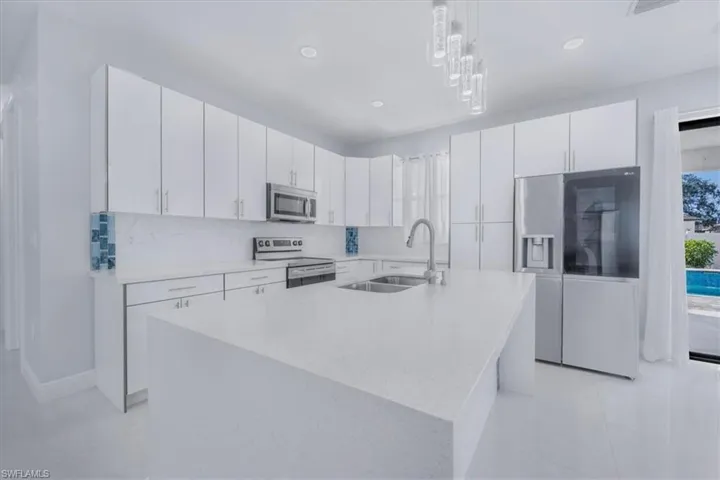 Kitchen featuring stainless steel appliances, light stone counters, a kitchen island with sink, white cabinetry, and hanging light fixtures