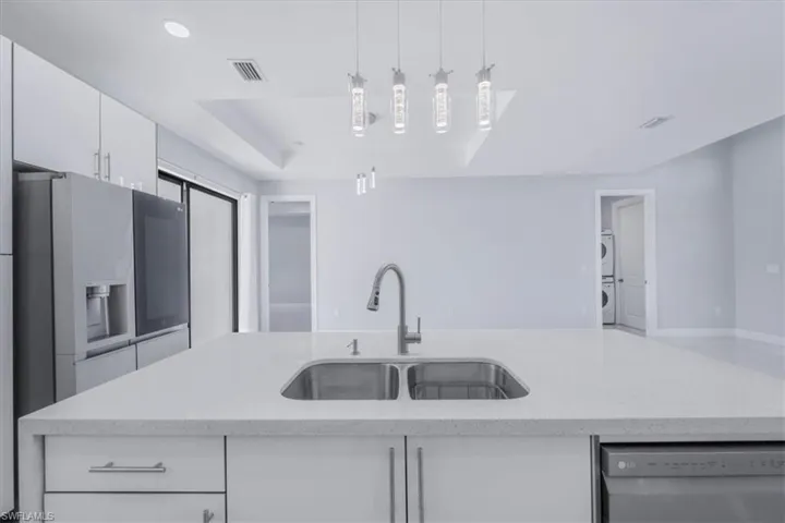 Kitchen featuring light stone countertops, white cabinets, appliances with stainless steel finishes, a center island with sink, and hanging light fixtures