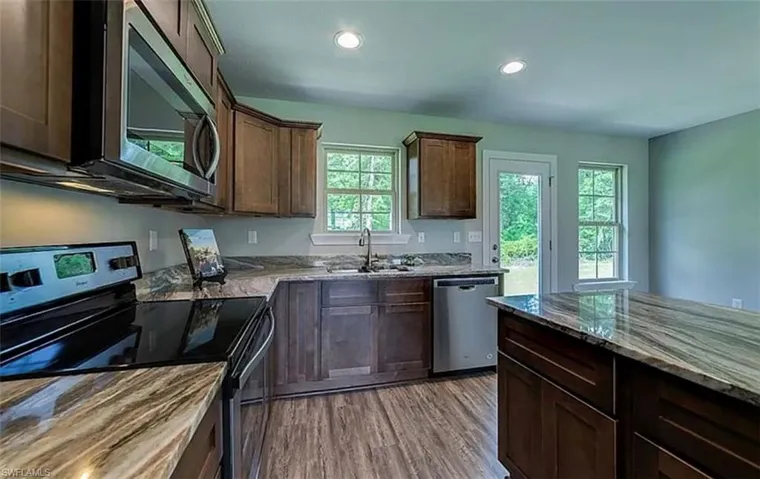 Kitchen featuring stainless steel appliances, dark wood-style flooring, dark brown cabinetry, recessed lighting, and dark stone countertops