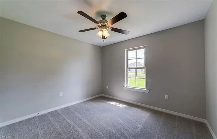 Carpeted empty room featuring baseboards and a ceiling fan
