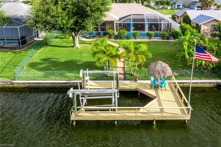 View of dock with glass enclosure, a water view, a lawn, and a swimming pool