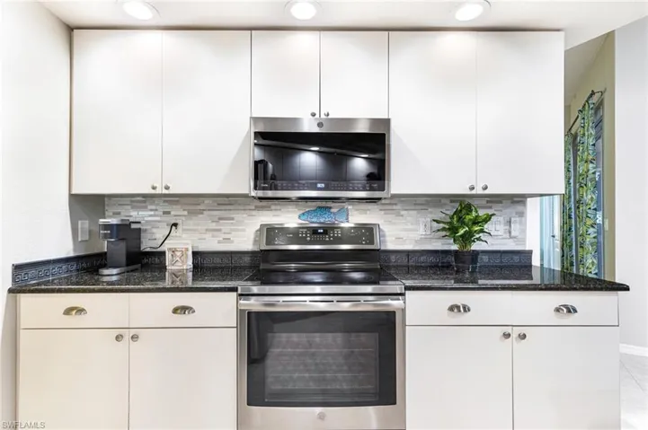 Kitchen featuring dark stone counters, white cabinetry, decorative backsplash, and stainless steel appliances