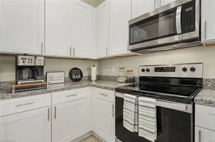 Kitchen featuring stainless steel appliances, white cabinetry, and light stone counters