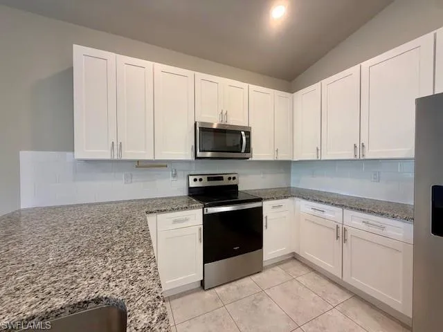 Kitchen featuring appliances with stainless steel finishes, light stone countertops, tasteful backsplash, white cabinets, and light tile patterned flooring