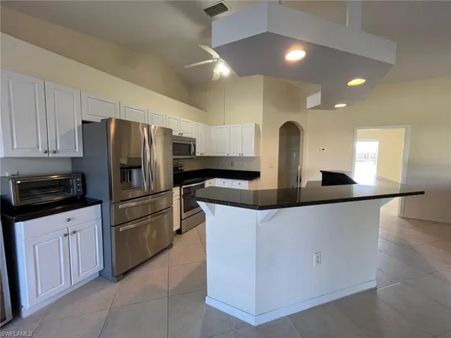Kitchen featuring a kitchen breakfast bar, white cabinets, a ceiling fan, stainless steel appliances, with additional decorative shelving.