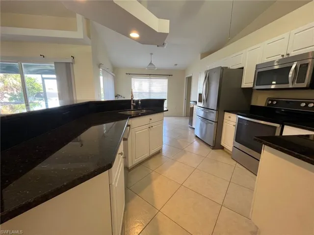 Kitchen featuring stainless steel. appliances, white cabinets, dark stone counters, lofted ceiling, and recessed lighting