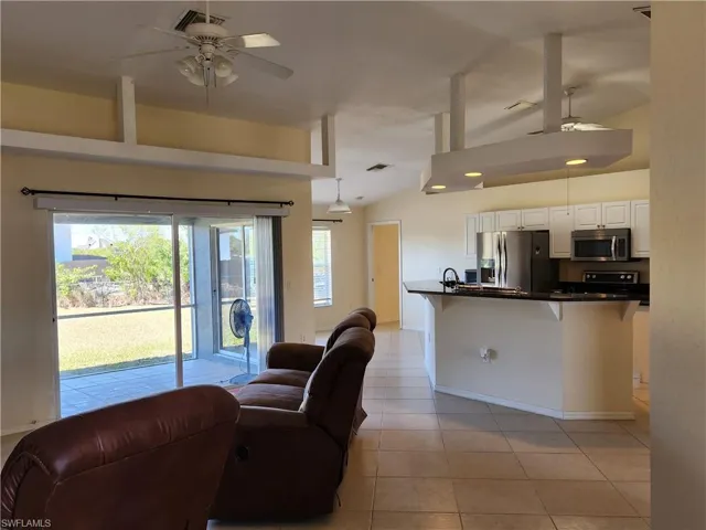 Living area with a ceiling fan, vaulted ceiling, and light tile floors throughout.