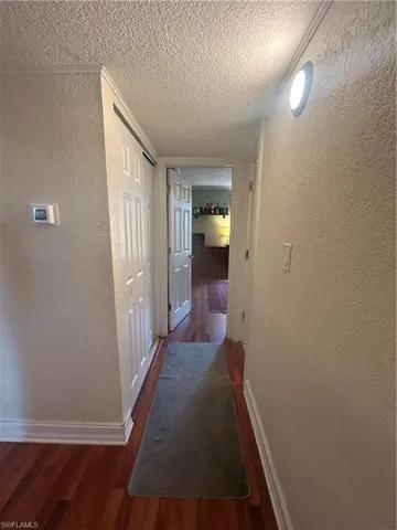 Hallway with a textured ceiling and dark hardwood / wood-style floors