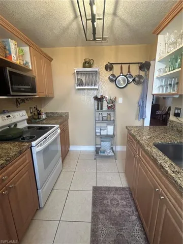 Kitchen featuring a textured ceiling, dark stone countertops, light tile flooring, and range
