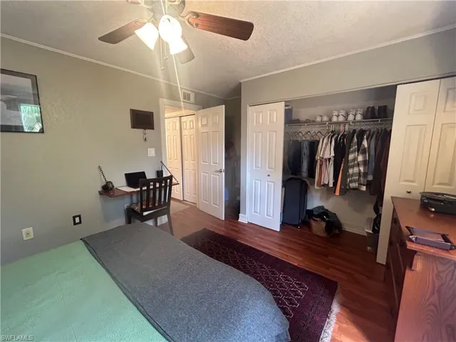 Bedroom with ceiling fan, a textured ceiling, ornamental molding, and wood-type flooring