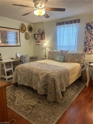 Bedroom with hardwood / wood-style floors, ceiling fan, and a textured ceiling