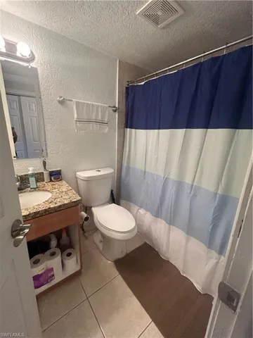 Bathroom with a textured ceiling, vanity, toilet, and tile floors