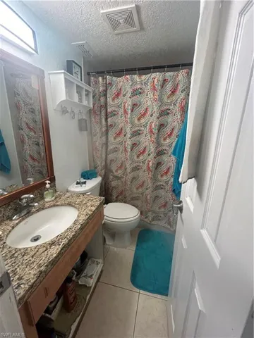 Bathroom featuring tile flooring, vanity, toilet, and a textured ceiling