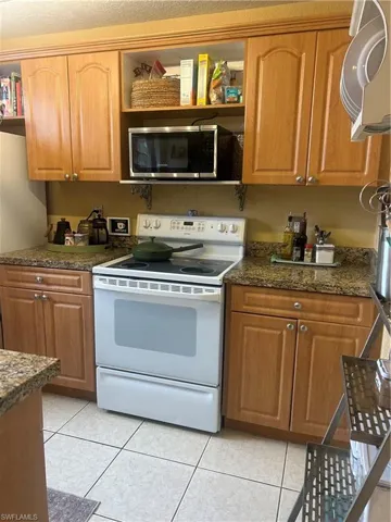 Kitchen featuring dark stone countertops, fridge, white electric range, and light tile floors