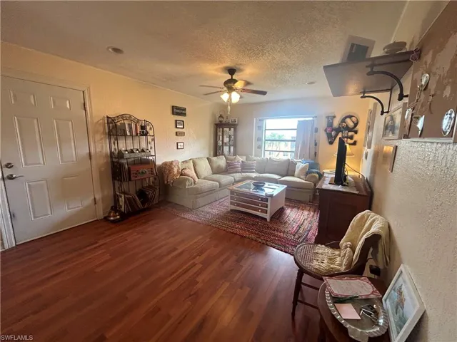 Living room featuring a textured ceiling, ceiling fan, and dark hardwood / wood-style flooring