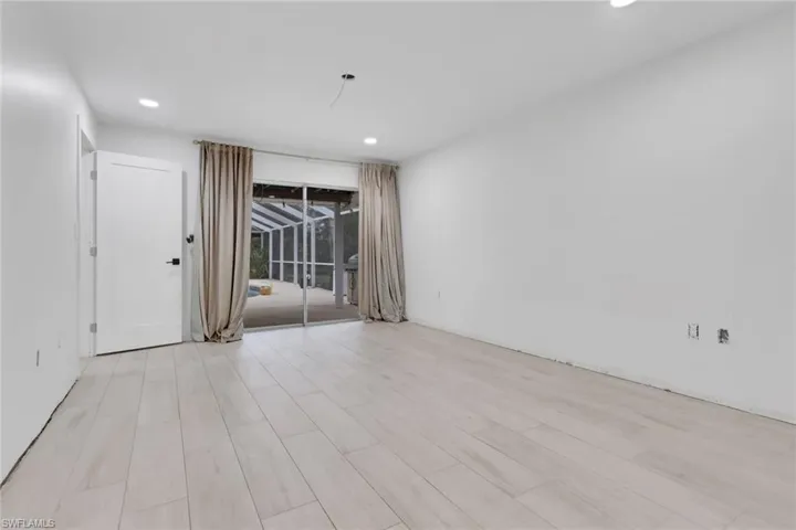 Spacious interior with light-tone wood-finish flooring, recessed ceiling lighting, and a sliding glass door opening to a screened outdoor area with a pool