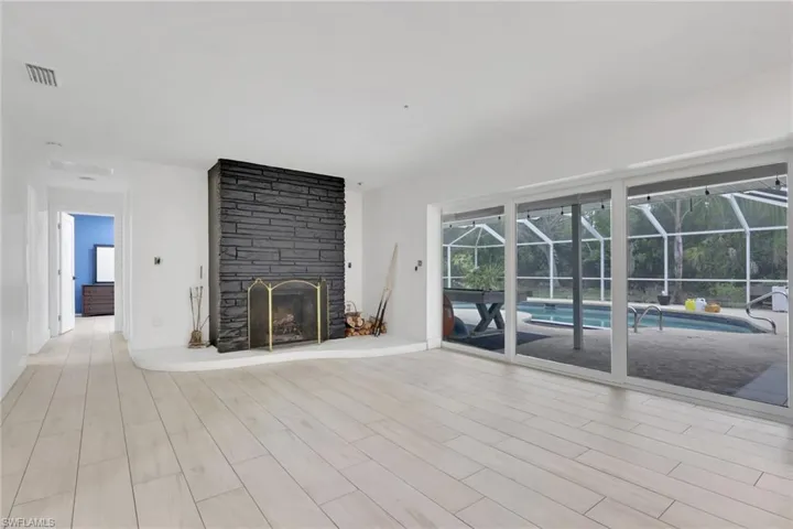 Spacious room featuring light wood-finish flooring, a stacked stone fireplace with a white hearth, and expansive sliding glass doors