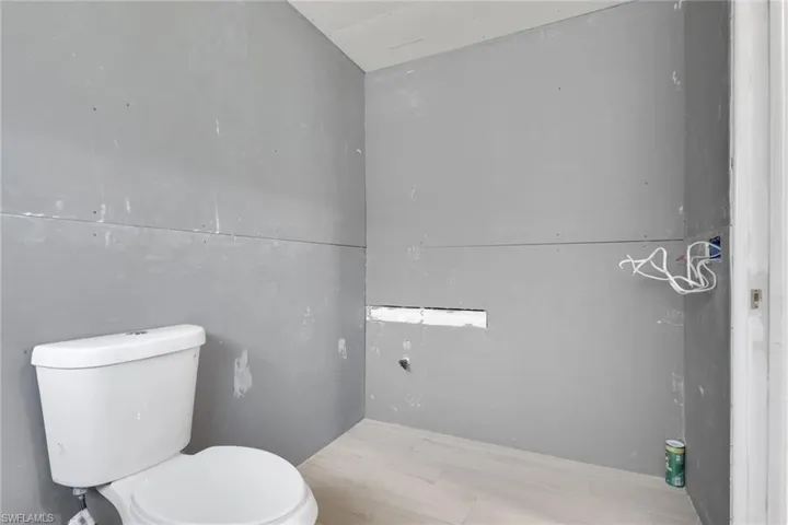 Powder room featuring a white two-piece toilet, light wood-finish flooring, and unpainted drywall walls