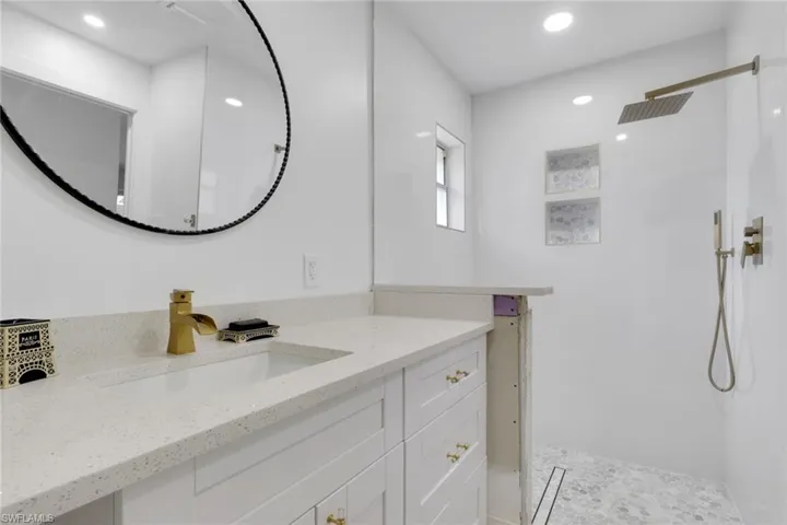 White vanity with a light speckled countertop, undermount sink, and brass-finish faucet